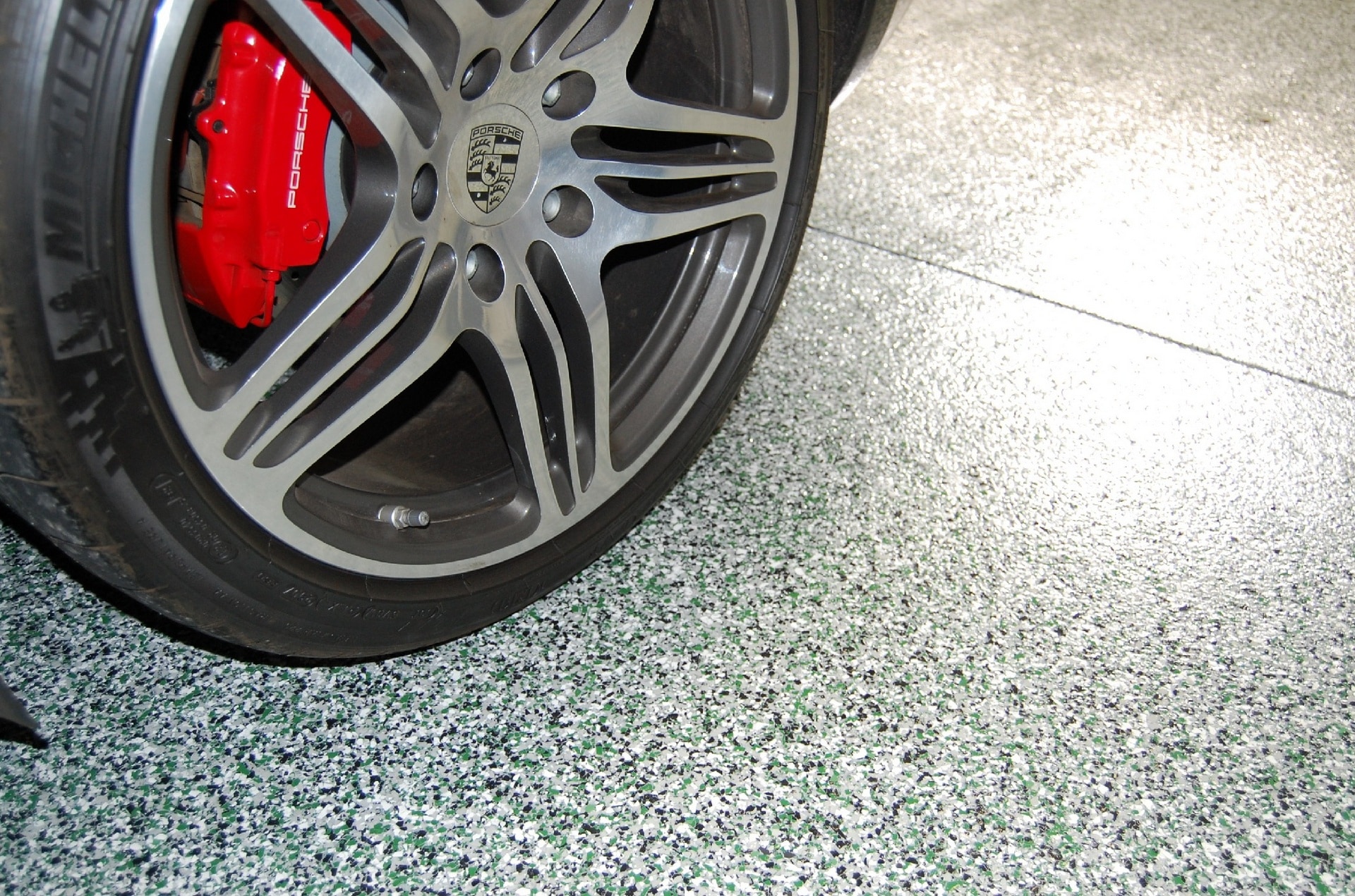 Porsche wheel resting on a gray and white flake epoxy garage floor installed by Brilliant Garage Floors